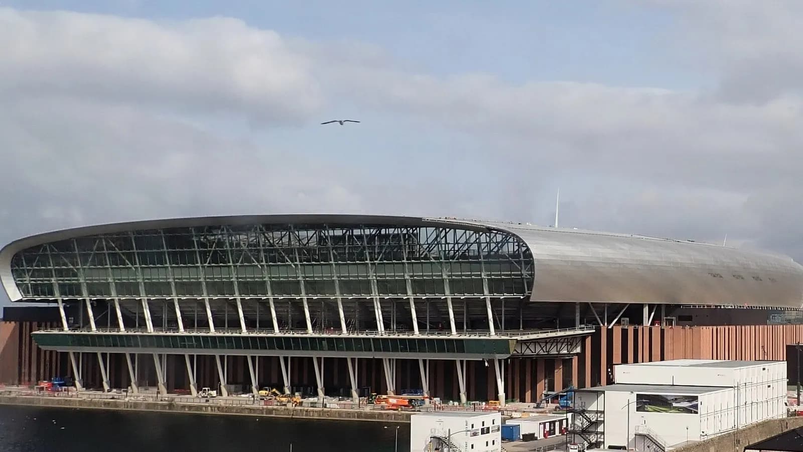 The glass-and-steel waterside facade of Everton's new stadium at Bramley-Moore Dock in Liverpool, still under construction beside the Mersey, photographed on 18 August 2024, a file photograph of the ground now called Hill Dickinson Stadium and not of Thursday night's match