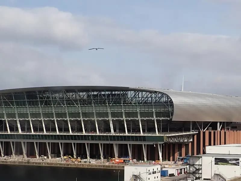 The glass-and-steel waterside facade of Everton's new stadium at Bramley-Moore Dock in Liverpool, still under construction beside the Mersey, photographed on 18 August 2024, a file photograph of the ground now called Hill Dickinson Stadium and not of Thursday night's match