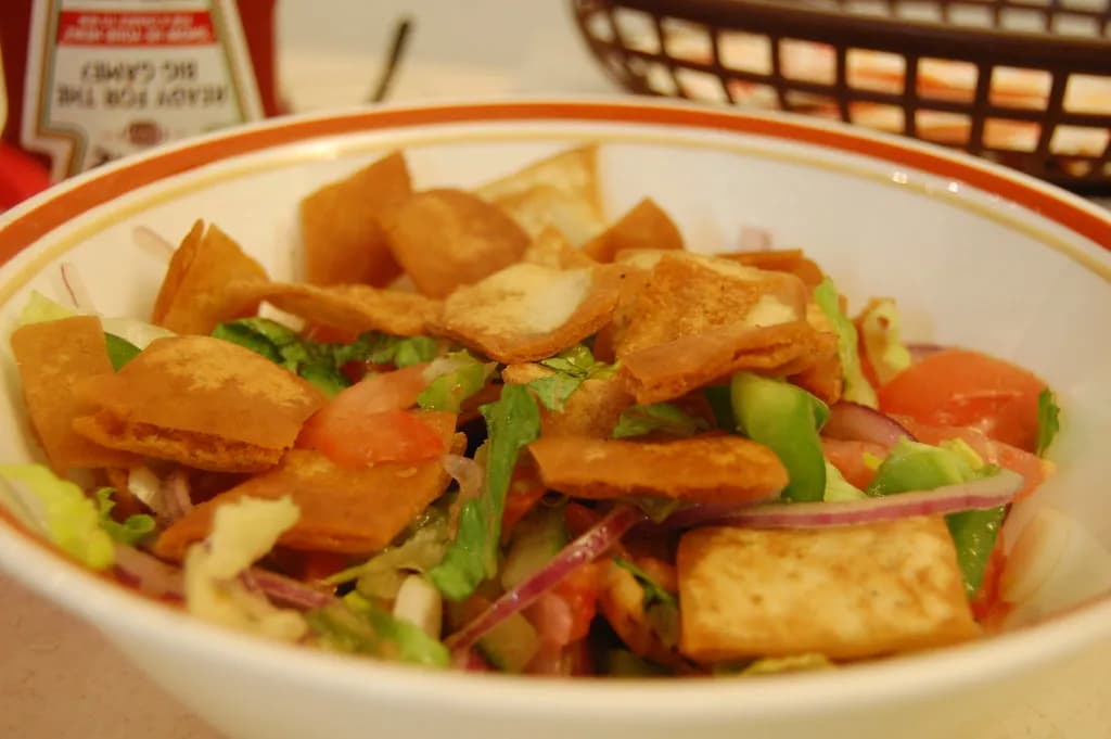 A vibrant bowl of fattoush salad with lettuce, tomatoes, cucumbers, and golden pita chips