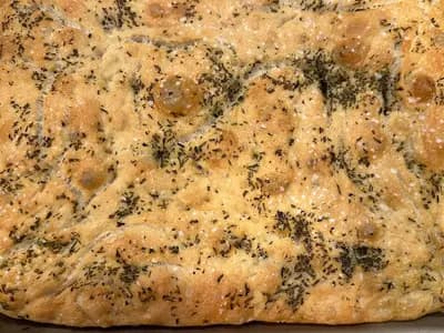 A homemade rosemary focaccia in a metal baking tray, dimpled and golden, baked in the United States and photographed in August 2024