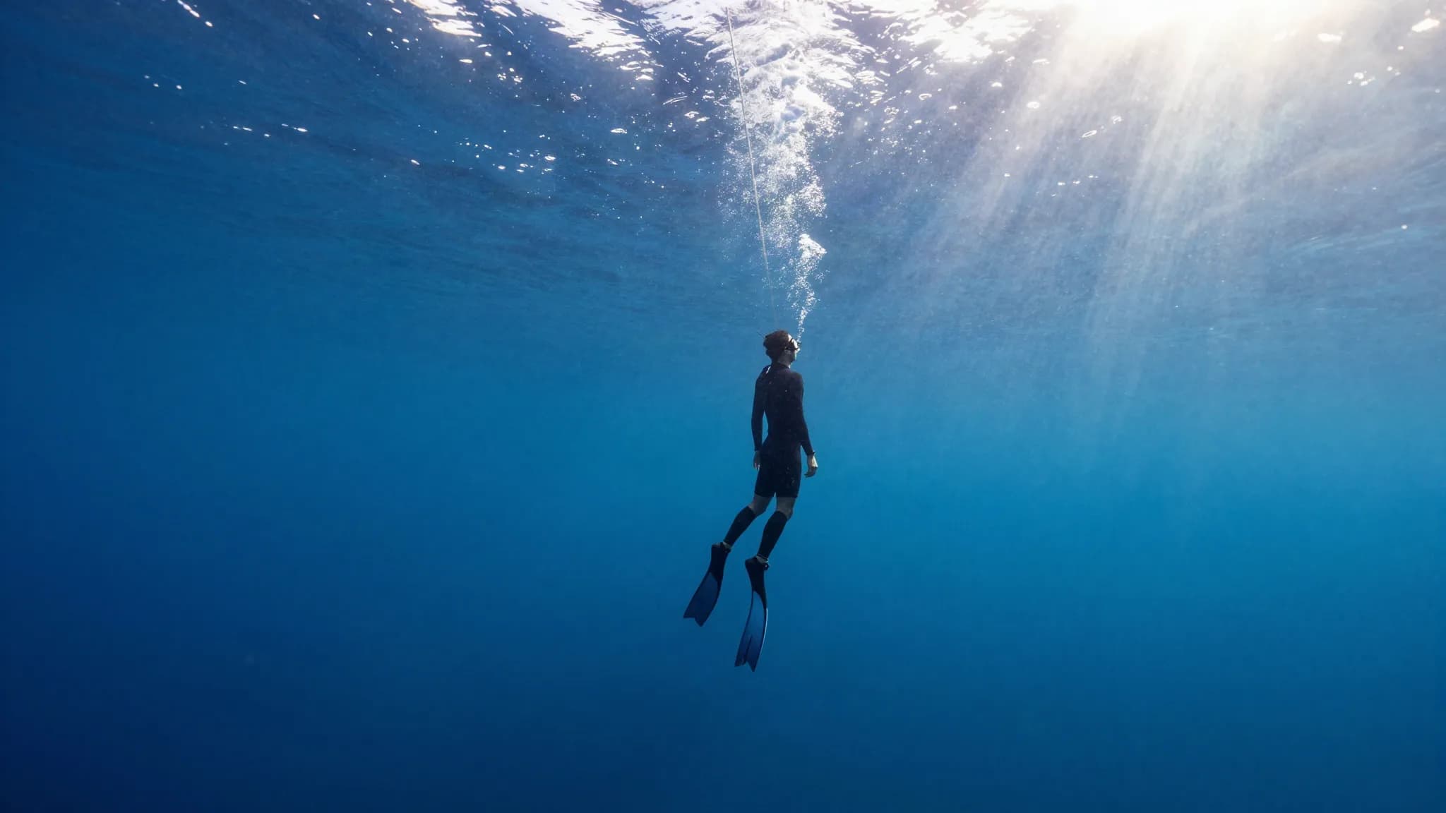 A freediver descending a guide rope into deep blue water