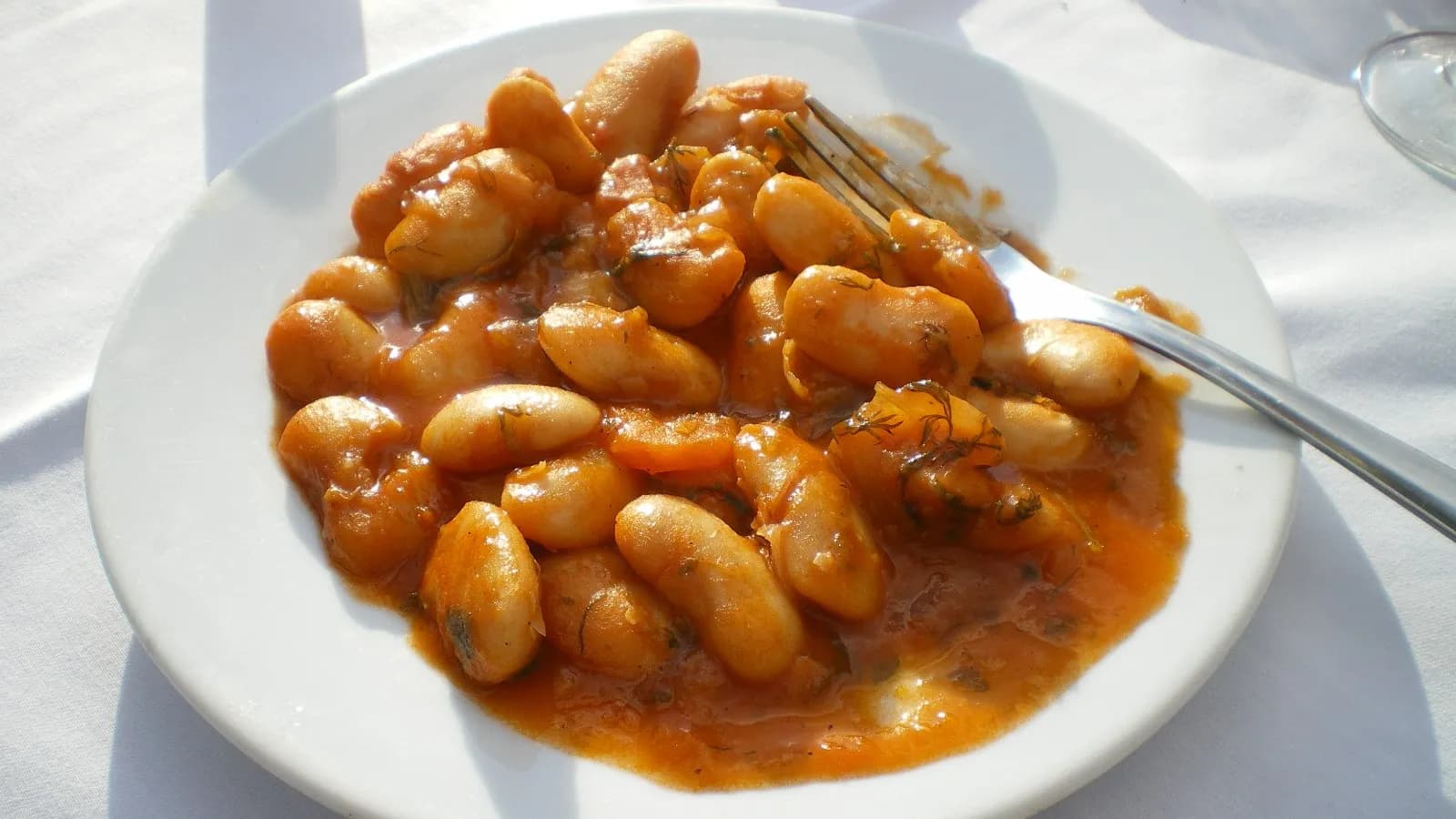 A plate of gigantes plaki, large white beans in a thick tomato and olive oil sauce, with a fork