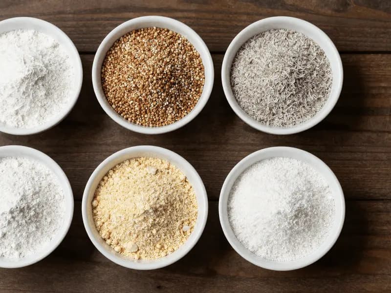 Small bowls of different gluten-free flours arranged on a wooden surface