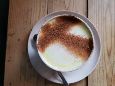 A cup of turmeric milk seen from above on a wooden table, dusted with ground spice across the foam