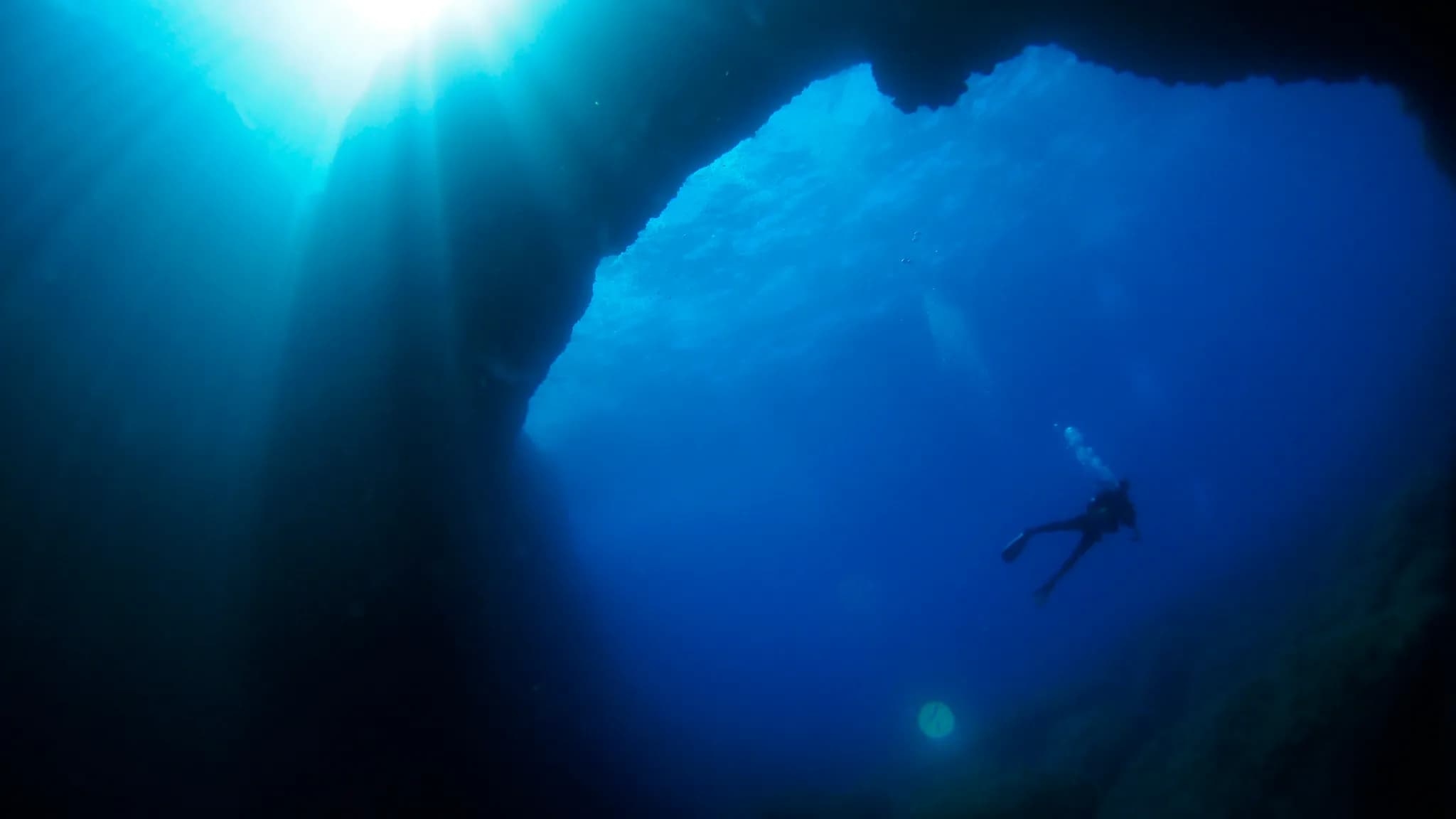 A scuba diver entering clear blue Mediterranean water beside the limestone coast of Gozo