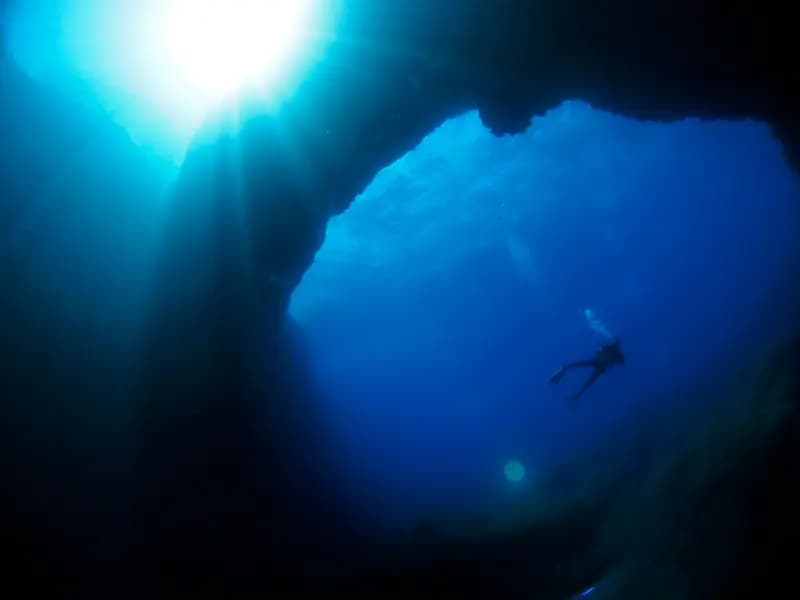 A scuba diver entering clear blue Mediterranean water beside the limestone coast of Gozo