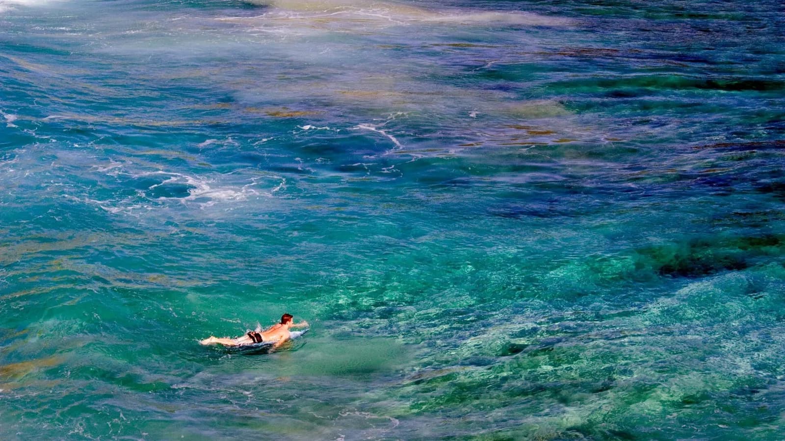 A surfer paddling out in a remote cove on Kauai where the shallow coral reef shows as bands of colour in the blue water, photographed on 7 January 2008 by the US Geological Survey, a file photograph of the island's reefs and not of the post-hurricane repair work