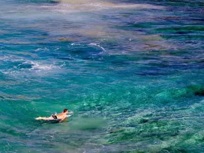 A surfer paddling out in a remote cove on Kauai where the shallow coral reef shows as bands of colour in the blue water, photographed on 7 January 2008 by the US Geological Survey, a file photograph of the island's reefs and not of the post-hurricane repair work