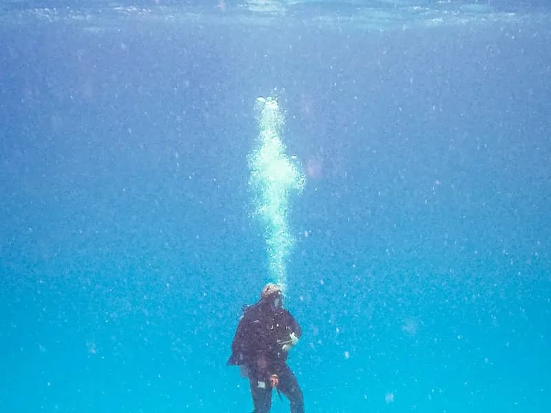 A scuba diver in a dark wetsuit rising through clear blue water with a column of bubbles above, photographed off Cozumel, Mexico, on 31 January 2016, a file photograph illustrative of diving and not of any case of the condition