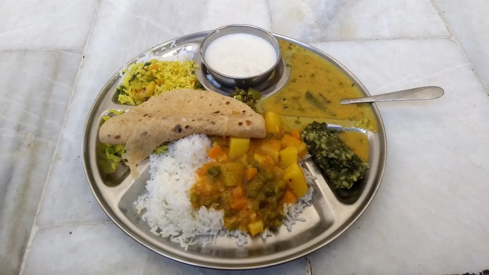 An Indian vegetarian thali of rice, dal, vegetable curry, chutney and flatbread on a steel plate. It is not a Jain meal, but it is the format one is served in
