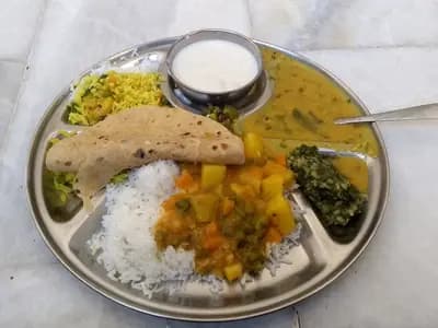 An Indian vegetarian thali of rice, dal, vegetable curry, chutney and flatbread on a steel plate. It is not a Jain meal, but it is the format one is served in