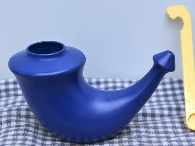 A blue ceramic neti pot with its measuring spoon, the shape used for pouring saline through one nostril and out of the other