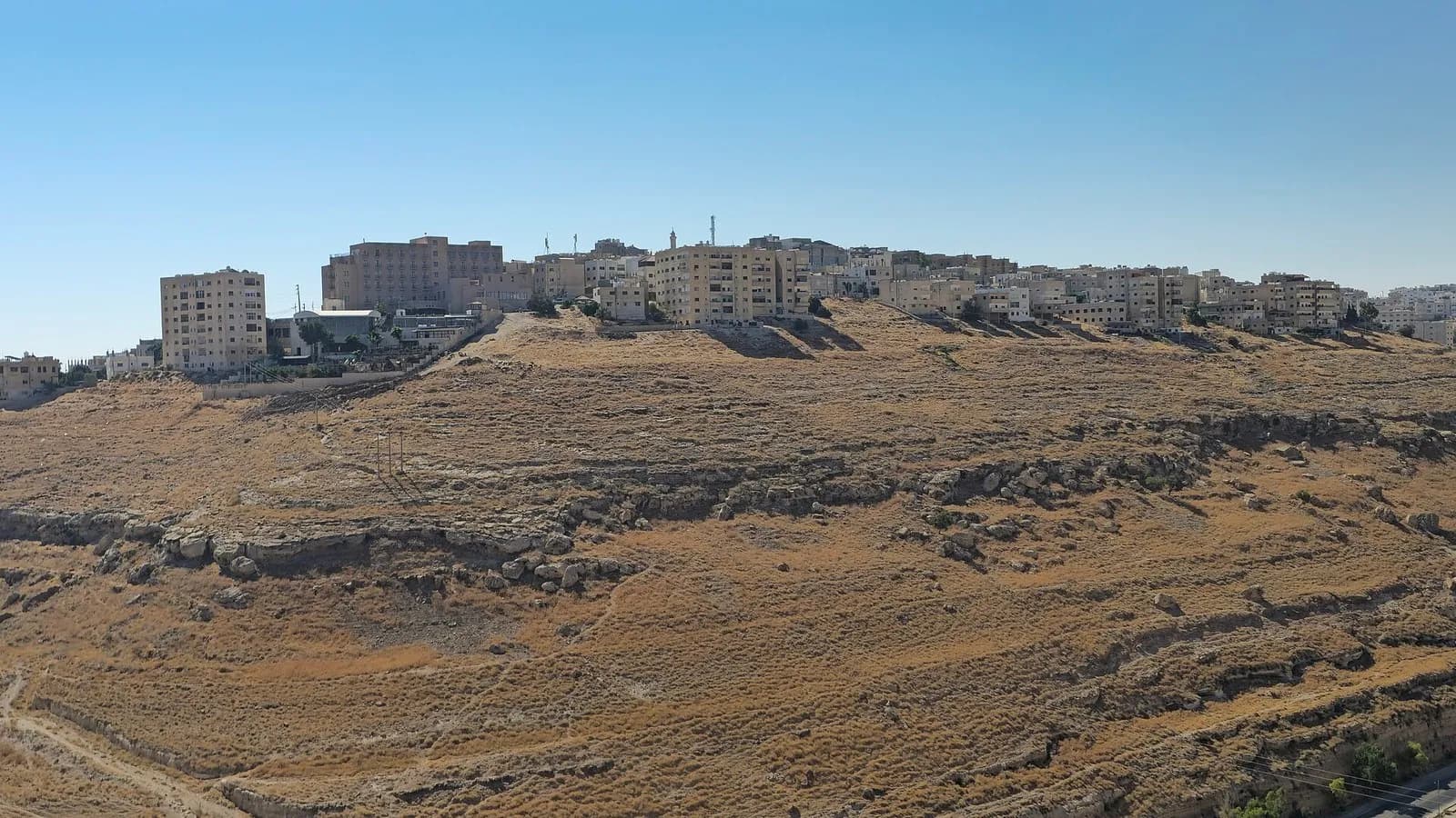 Buildings along a ridge in the city of Al-Karak above a dry hillside under a clear sky, photographed on 9 August 2026, a file photograph illustrative of the city and not of the church or the attack