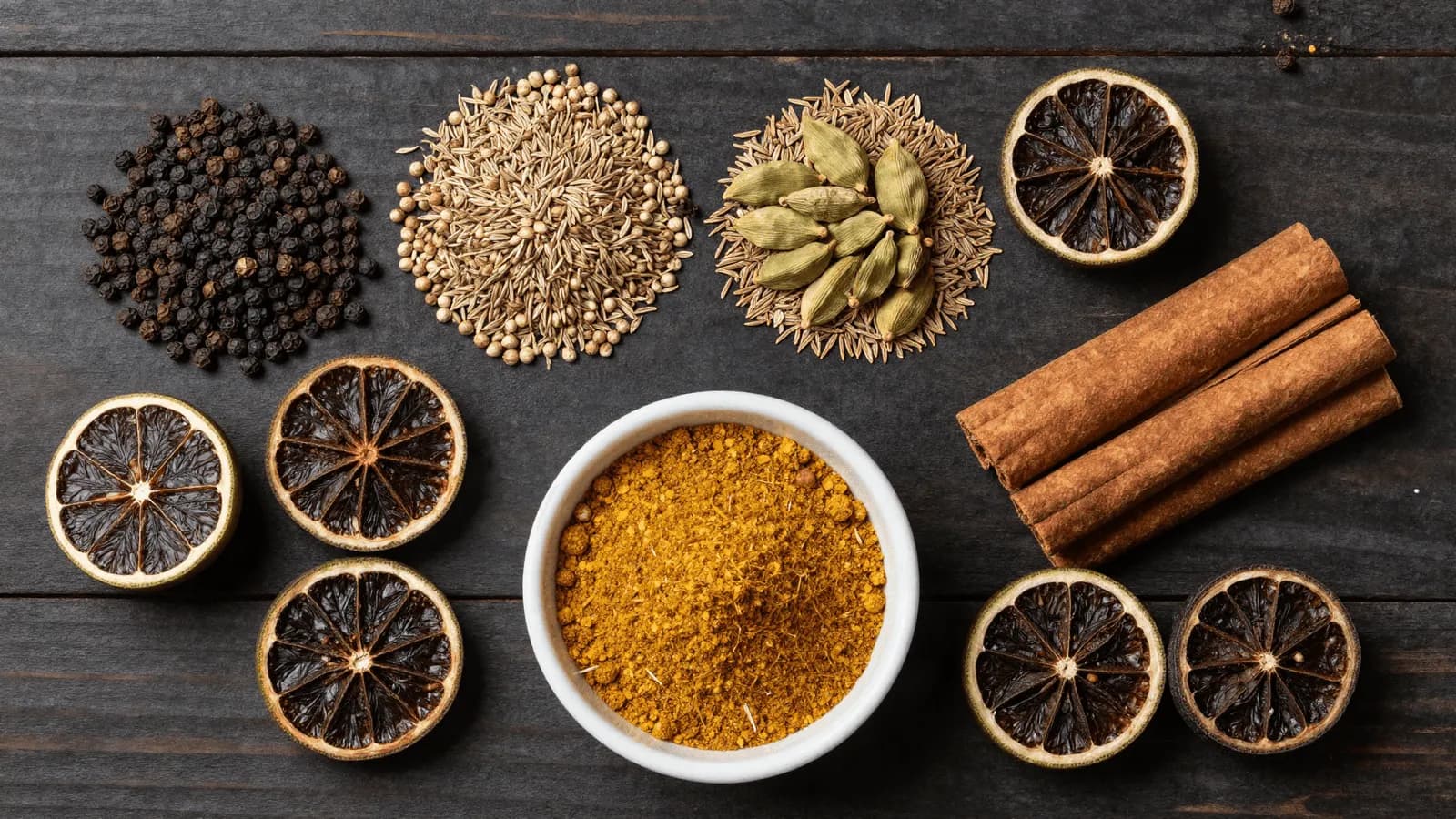 Whole spices and dried black limes beside a bowl of freshly ground kabsa blend