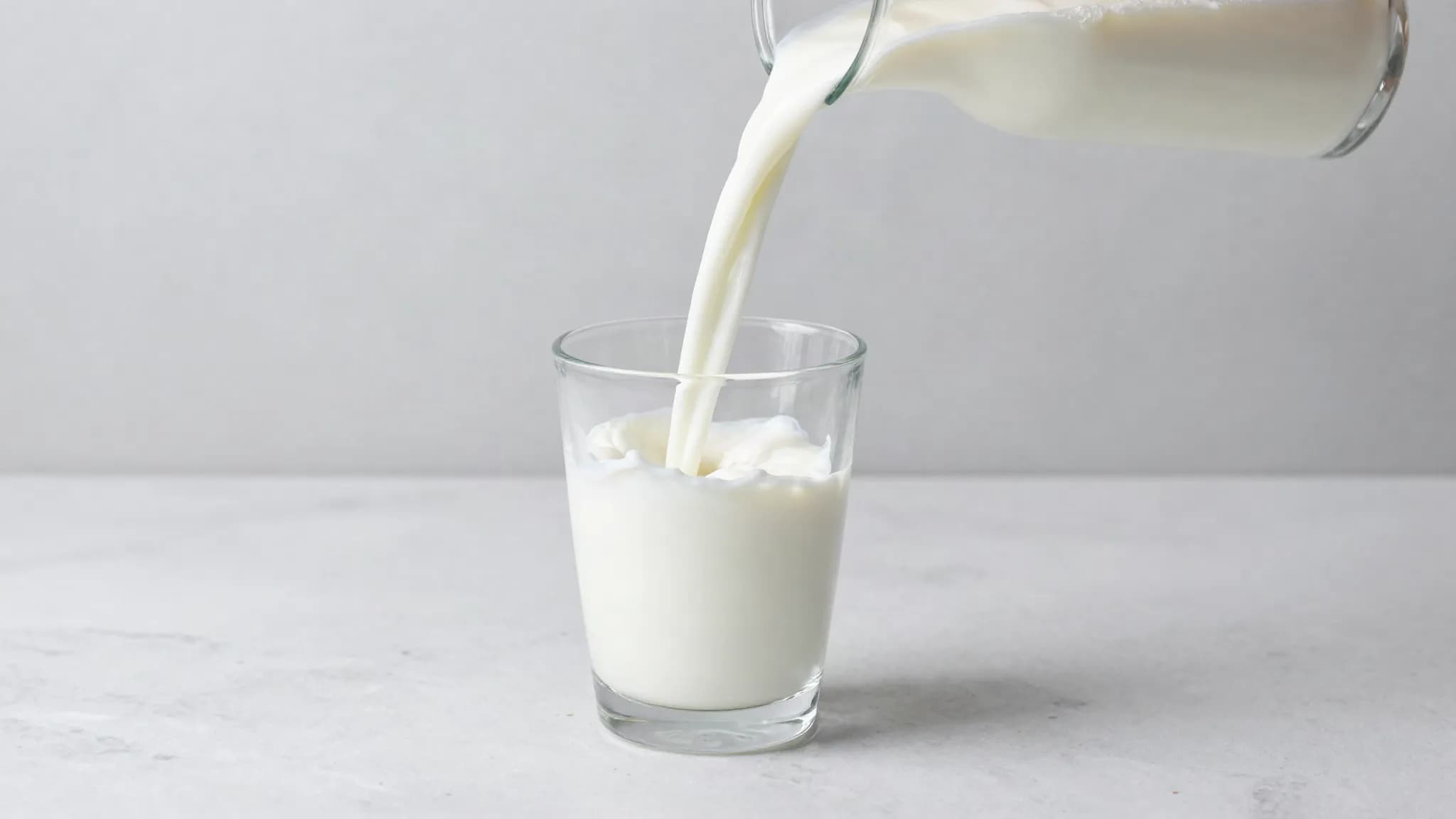 Milk being poured into a glass on a marble counter