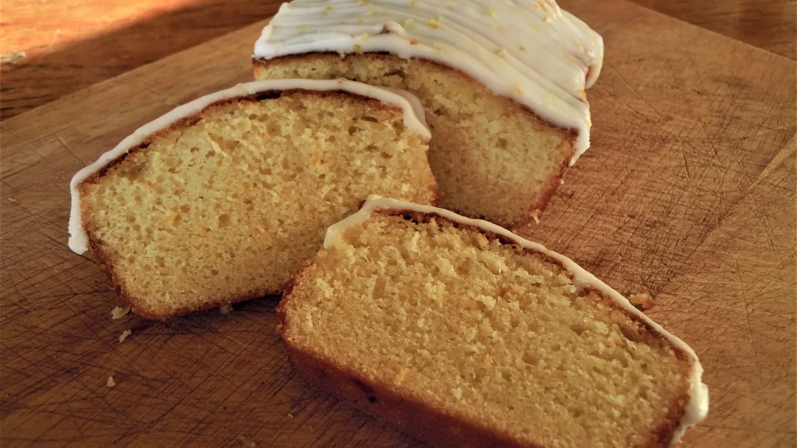 A sliced lemon drizzle loaf cake with a white glaze on a wooden board, photographed in Norfolk, England in January 2010