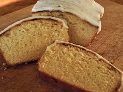 A sliced lemon drizzle loaf cake with a white glaze on a wooden board, photographed in Norfolk, England in January 2010