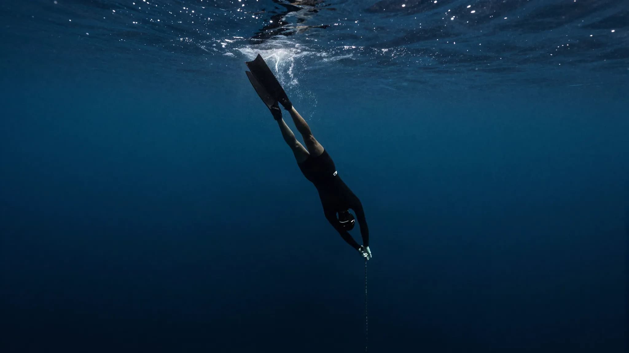 A freediver descending into dark deep water where the light fades