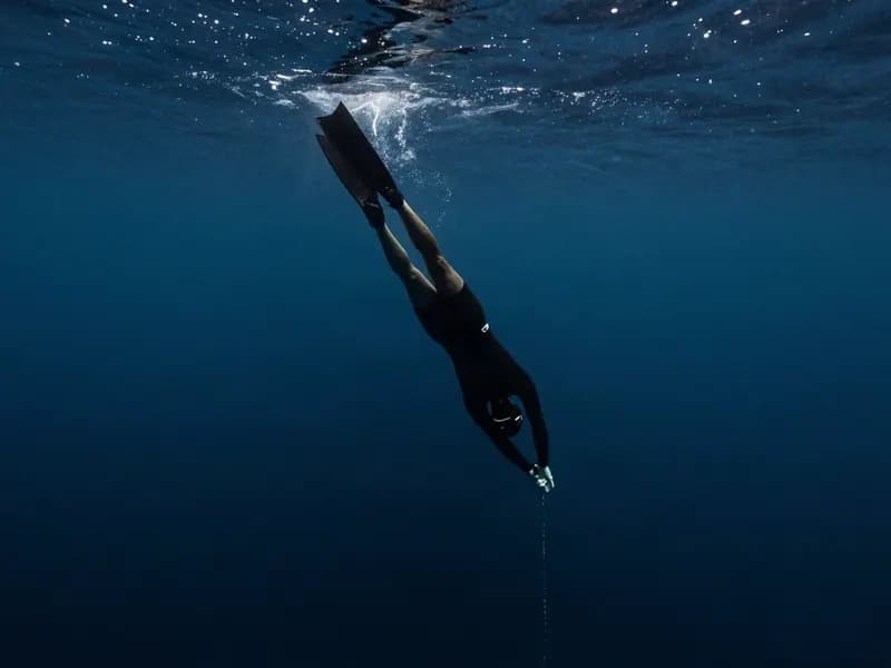 A freediver descending into dark deep water where the light fades