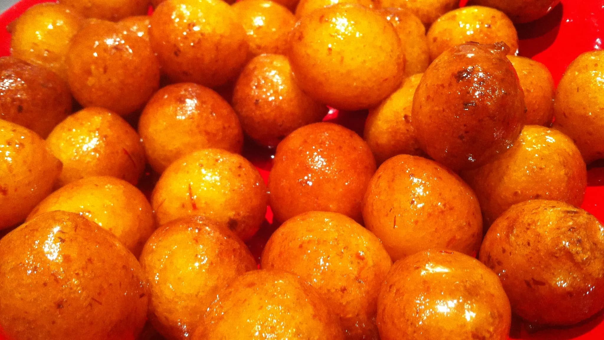 A plate of small round golden fried dumplings glazed with dark date syrup and sesame seeds