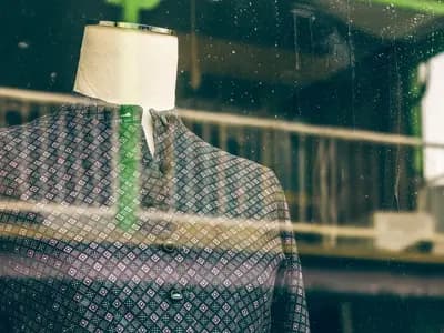 A mannequin in a jacket seen through a shop window, with the street reflected in the glass