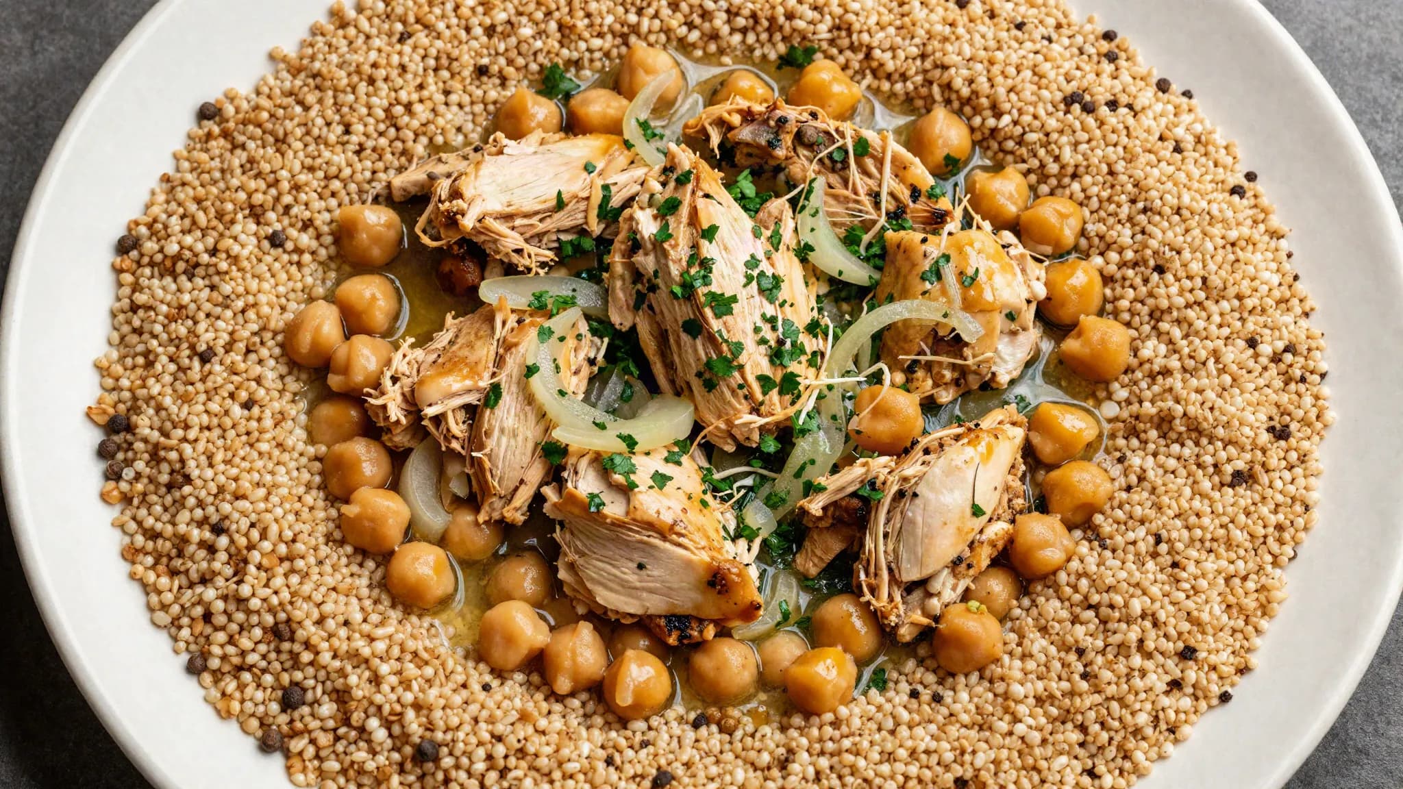 A platter of maftoul topped with chicken, chickpeas and parsley