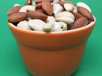 A small terracotta pot filled with almonds and cashews against a green background, two of the nut sources of magnesium, photographed in June 2018