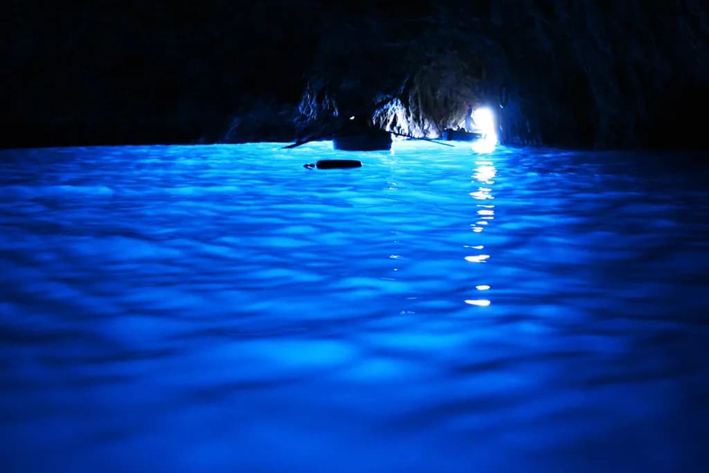 A technical diver silhouetted at the entrance of a deep underwater cave, lit by a dive torch
