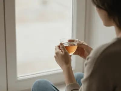A person sitting quietly by a window in early morning light with a cup of tea