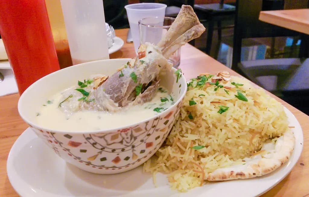 Large serving platter of mansaf with turmeric rice, tender lamb in creamy jameed yogurt sauce, toasted almonds, and fresh parsley garnish