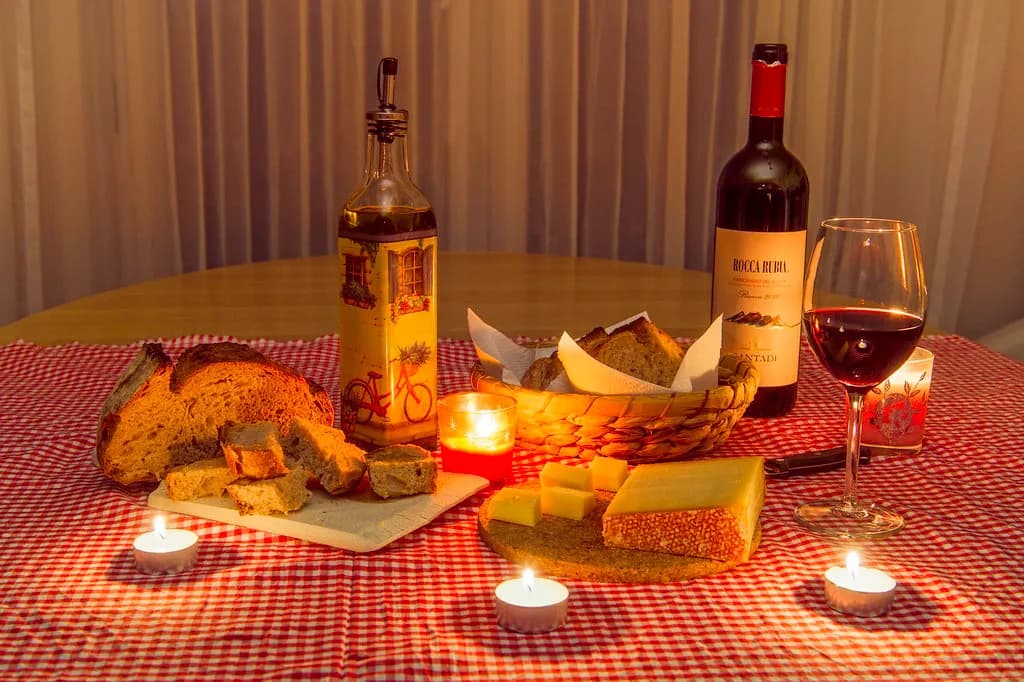 A rustic table with a bottle of olive oil, crusty bread, tomatoes and a bowl of mixed nuts