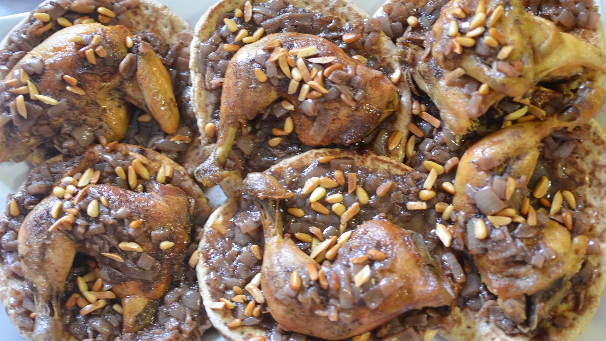 Roast chicken pieces on flatbread piled with dark red sumac onions and pine nuts