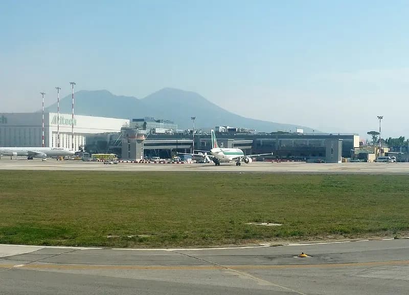 The apron and terminal buildings of Naples Capodichino airport with airliners at their stands, a light tower and the slopes of Vesuvius in the haze behind, photographed on 15 October 2011, a file photograph of the airport and not of the runway works