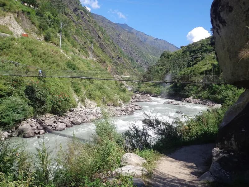 The Trishuli river running fast through a steep, narrow Himalayan valley in Nepal, with a footbridge crossing it