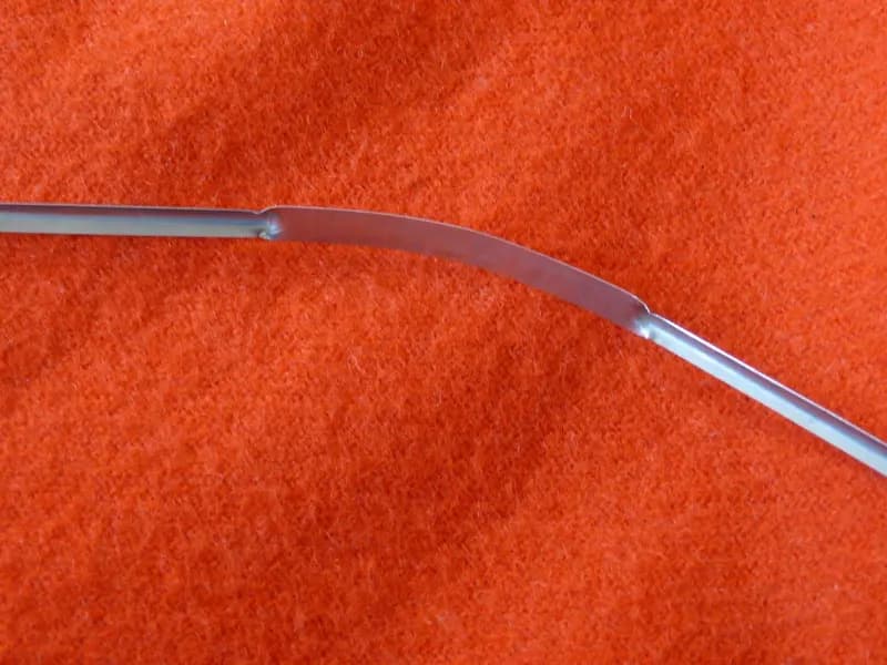A stainless steel tongue scraper, the curved blade drawn from the back of the tongue forwards