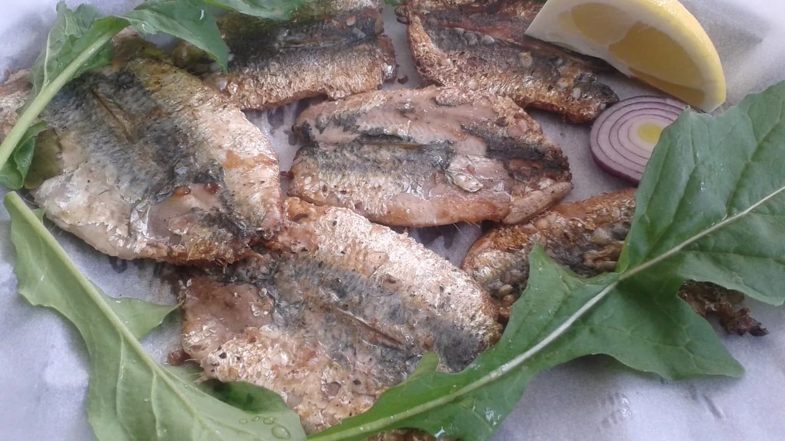 Grilled sardines served with a lemon wedge, red onion and green leaves, photographed in March 2017