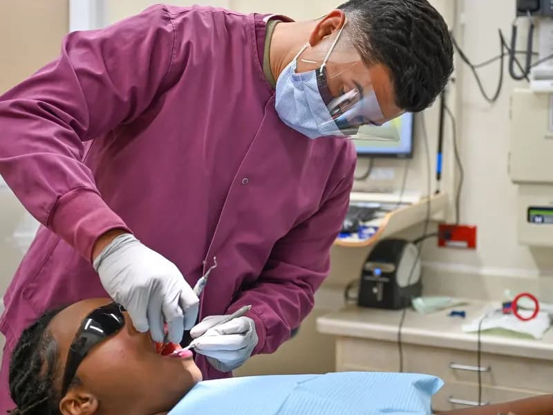 A dental technician in a mask and gloves carrying out an oral examination on a patient lying in a dental chair