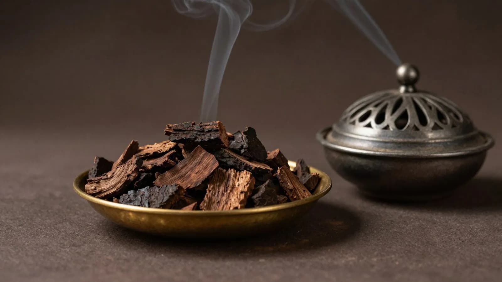 Dark aromatic oud wood chips beside a traditional incense burner