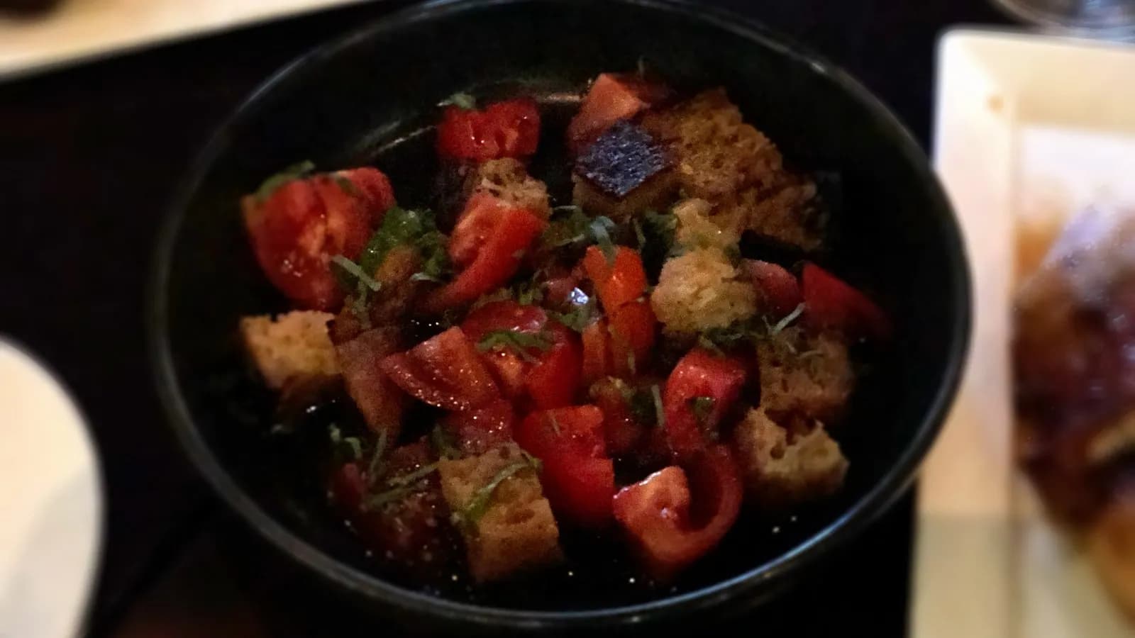 A dark bowl of panzanella, chunks of ripe tomato and toasted bread tossed with herbs and dressed in oil