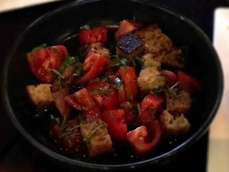 A dark bowl of panzanella, chunks of ripe tomato and toasted bread tossed with herbs and dressed in oil
