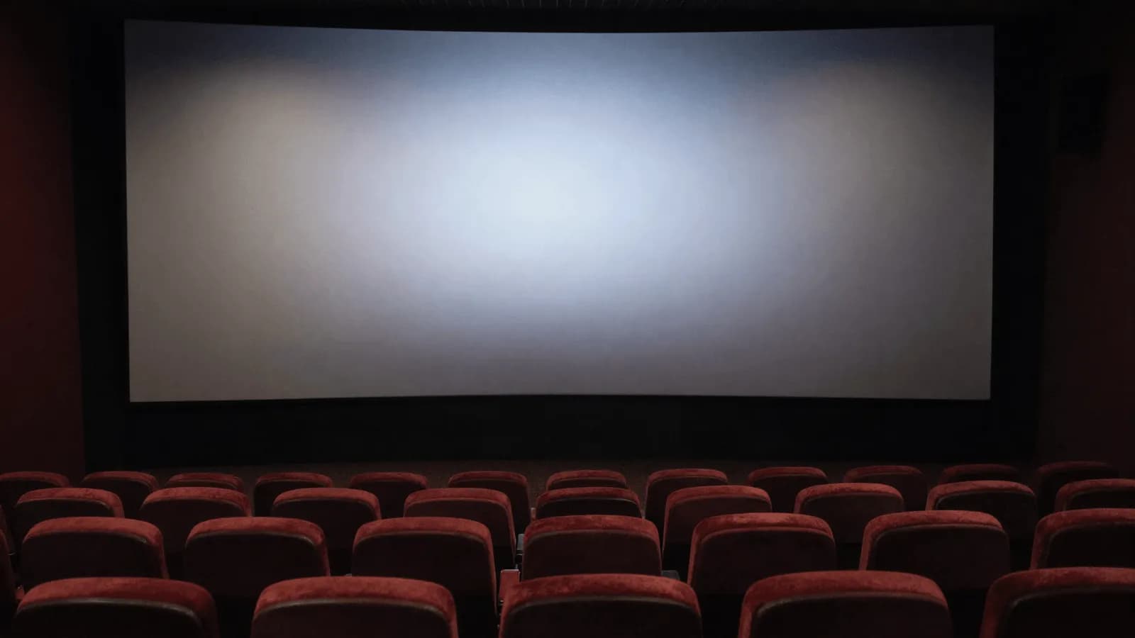 An empty cinema auditorium with rows of seats facing a blank screen