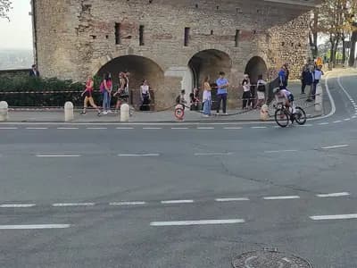 A lone cyclist rounding a bend beneath an old stone wall with spectators and a police motorcycle beside the road, photographed during Il Lombardia on 7 October 2023, a file photograph of the race and not of Paul Seixas or of Saturday's finish