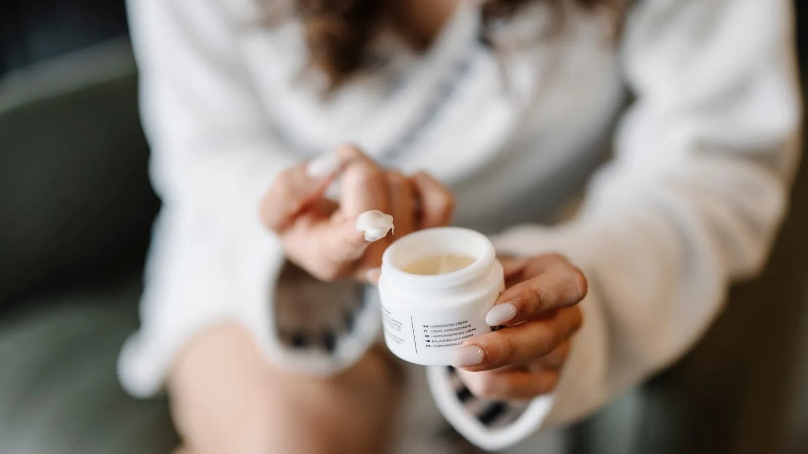 A person applying cream from a cosmetic jar
