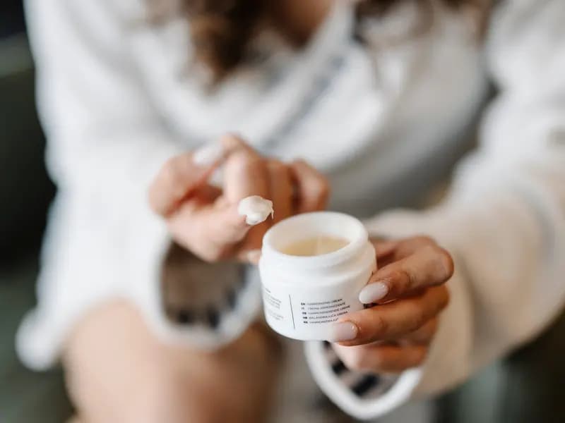 A person applying cream from a cosmetic jar