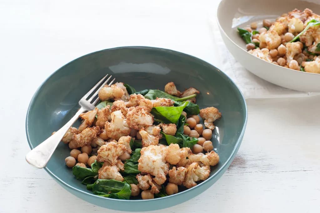 A wooden table with bowls of legumes, tofu, nuts and grilled protein representing plant and animal protein sources
