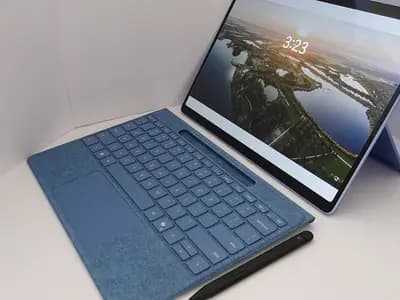 A blue tablet-style laptop with a detachable keyboard and a pen resting in front of it, its screen showing a landscape lock screen, photographed on 10 October 2024, a file photograph illustrative of a laptop and not of Flint or any Recursive product