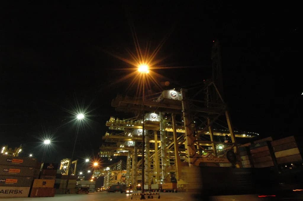 Container ship loaded with cargo, viewed from a Gulf port with cranes in the background