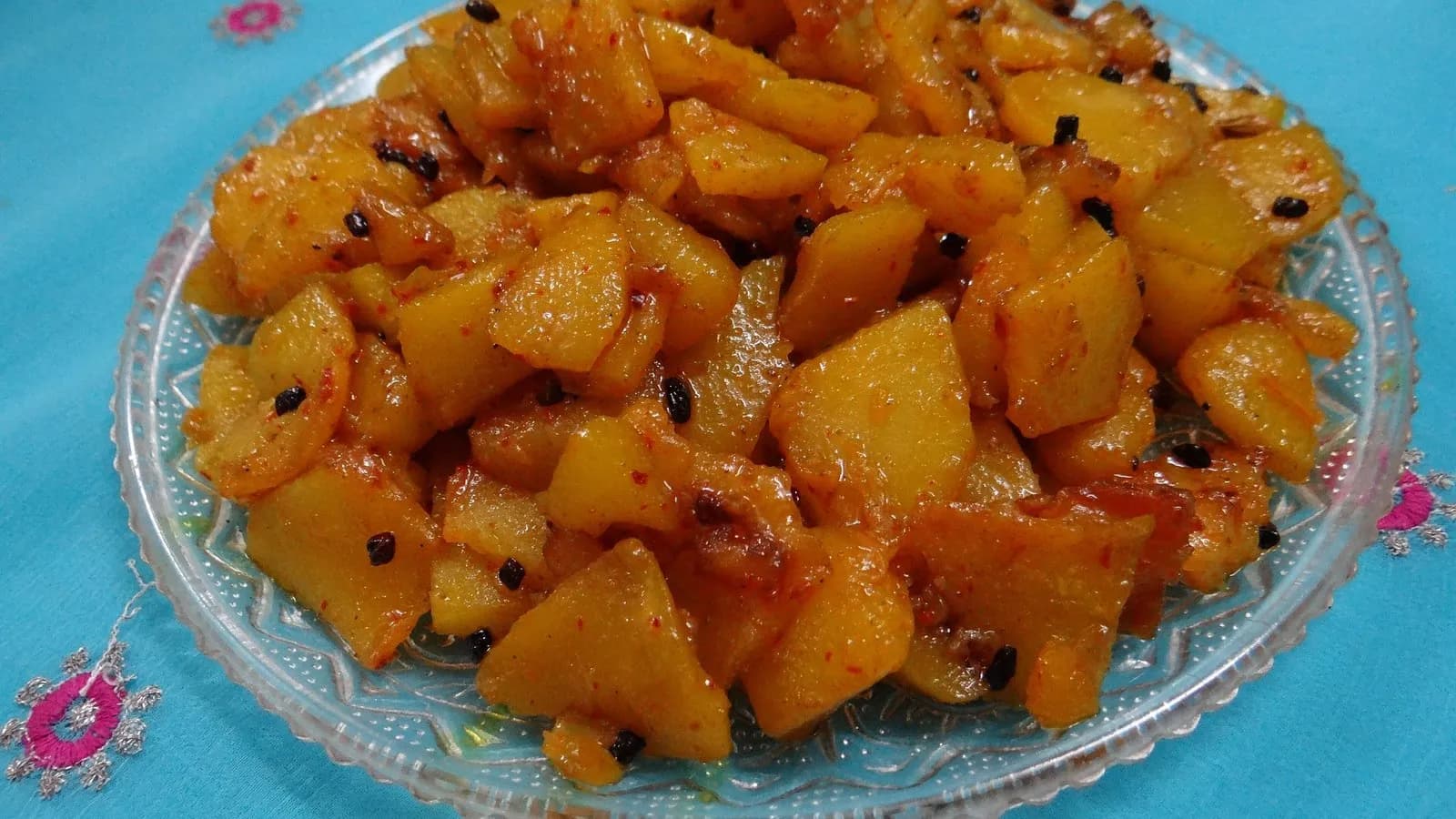 Pumpkin curry, kaddu ki sabzi, served on a glass plate with whole spices visible among the softened cubes
