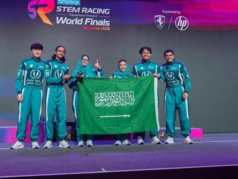 Members of Saudi Team Lynx in their green racing suits holding the flag of Saudi Arabia on the stage of the Aramco STEM Racing World Finals in Singapore, October 2026, a photograph supplied by Ithra