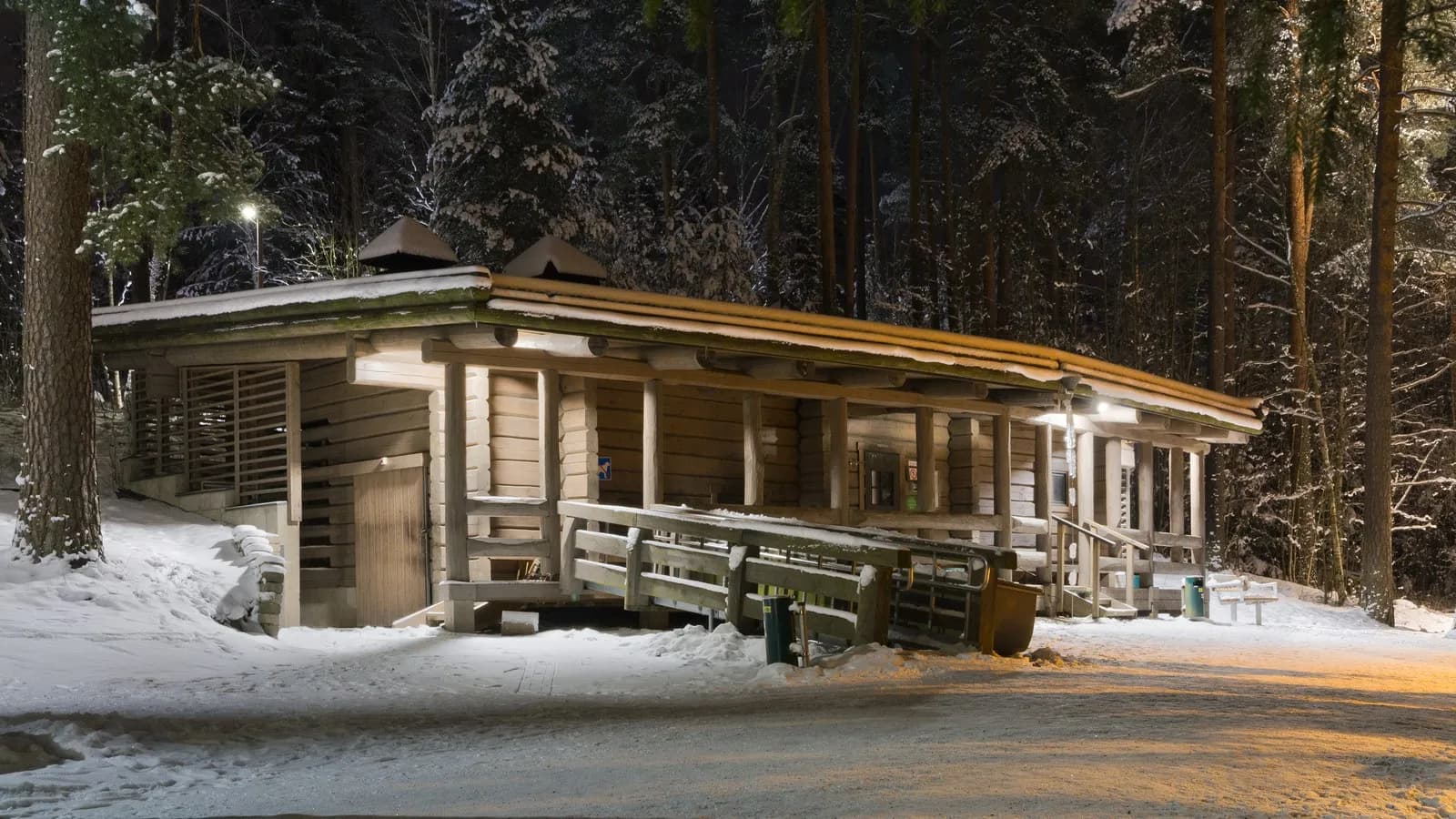 The public smoke sauna at Kuusijärvi in Vantaa, Finland, its timber walls lit at night with snow on the ground and the forest behind